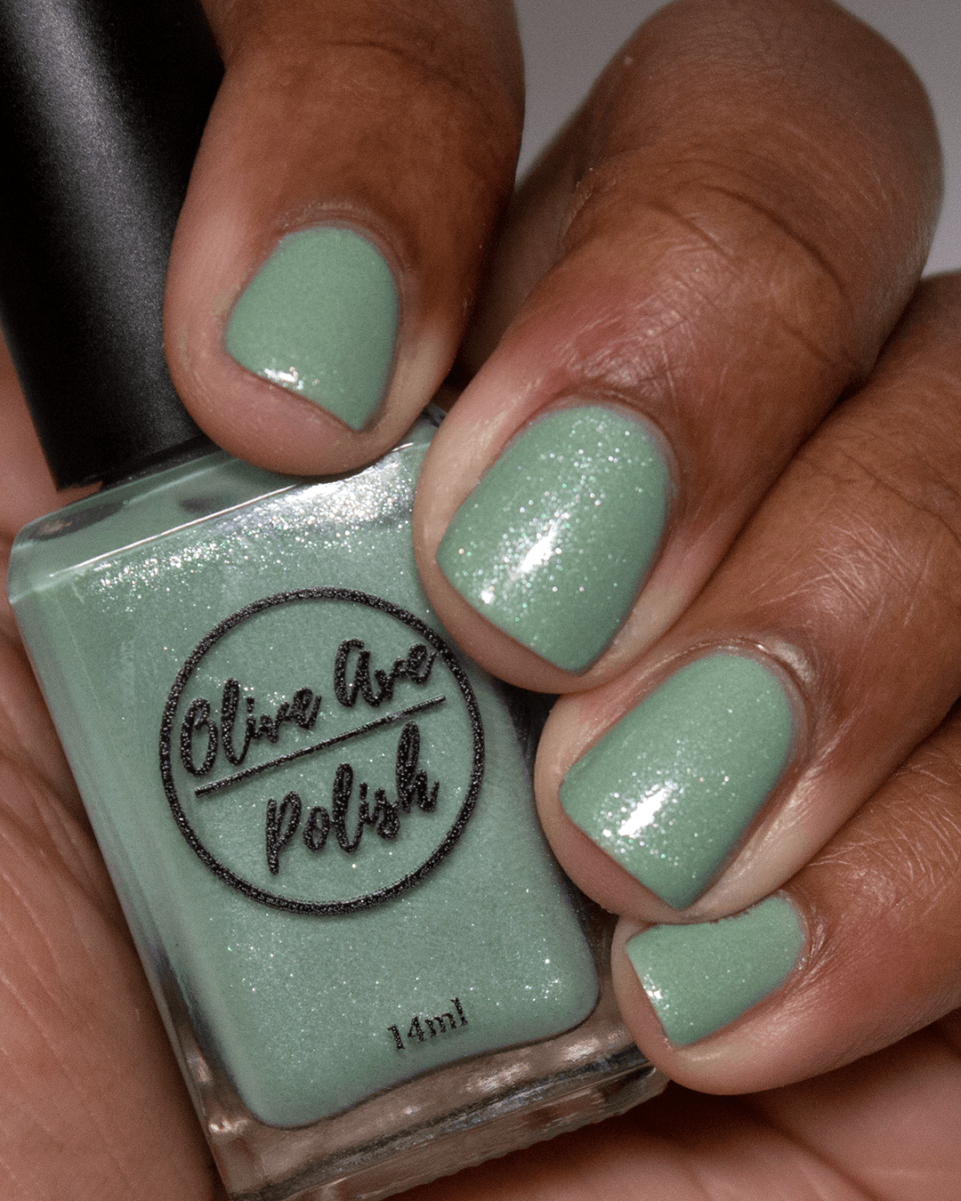 sage green shimmery nail polish swatch on medium skin tone