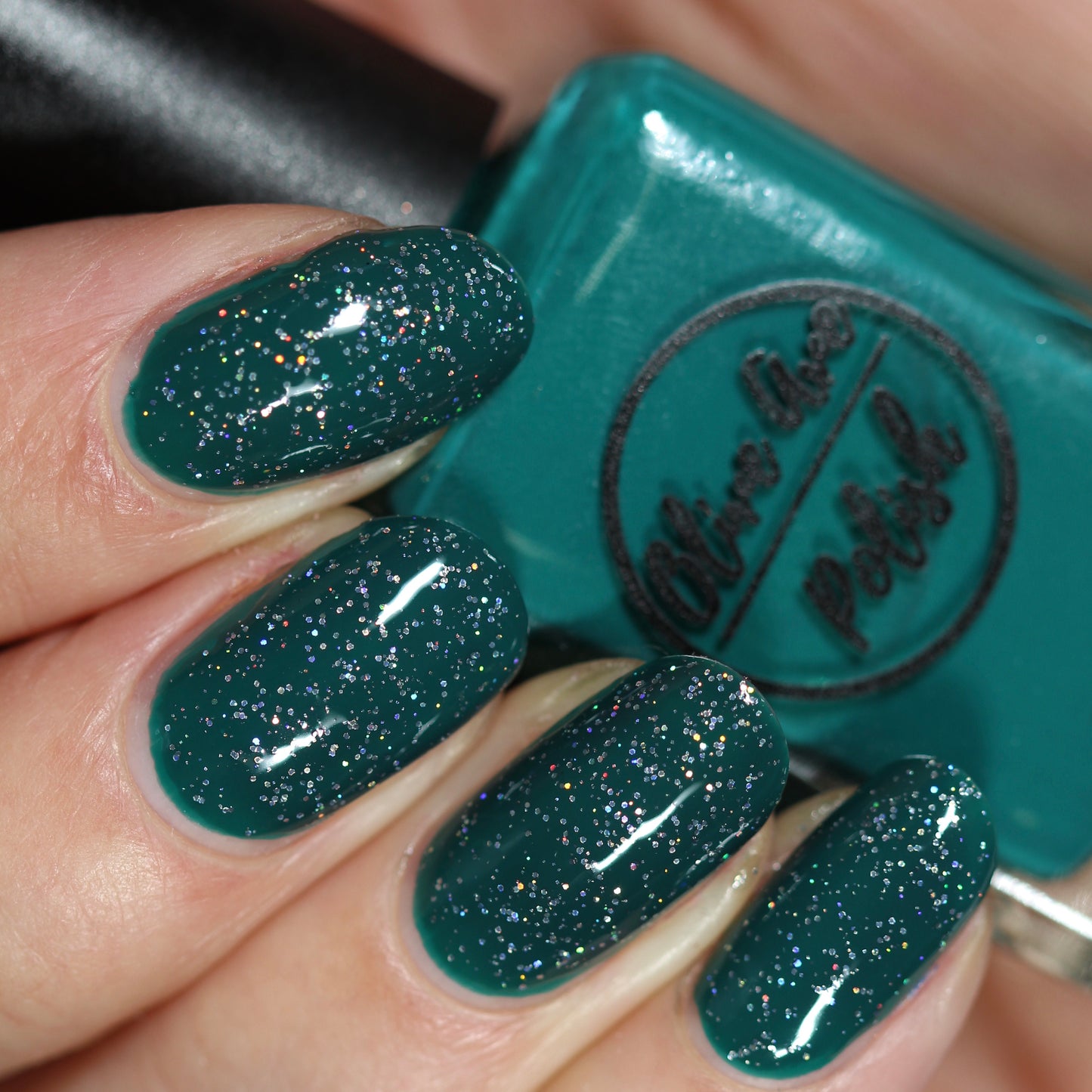 Black holographic nail polish layered over green polish swatch on pale skin tone