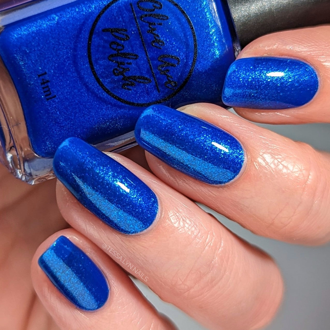 Blue glitter nail polish swatch on pale skin tone