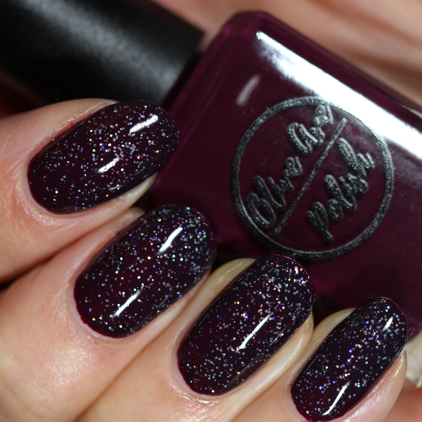 Black holographic nail polish layered over red polish swatch on pale skin tone